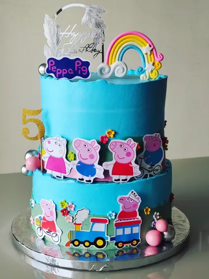 A two-tiered Peppa Pig cake that's full of joy. I used a bright blue buttercream and decorated it with the whole Peppa Pig family, a rainbow, and a choo-choo train for a playful and happy birthday.