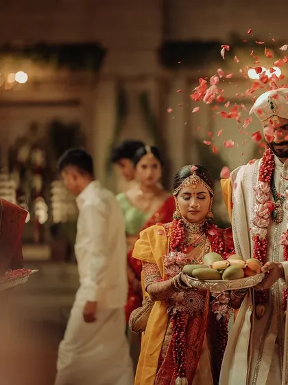 A candid moment during the wedding procession. The bride and groom, holding a tray of offerings, walk together in a moment that is both solemn and beautiful.