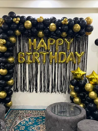 A closer view of the black and gold living room setup, highlighting the full balloon arch and the shiny foil "Happy Birthday" letters.