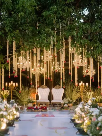 An enchanting evening wedding setup under a mango tree, adorned with hanging jasmine garlands and crystal chandeliers for a traditional yet elegant Bunt wedding.
