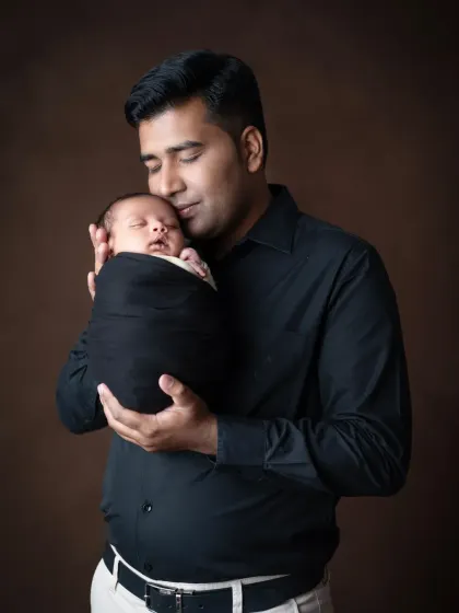 A father gently holds his sleeping newborn close to his cheek, a portrait of pure love and connection.