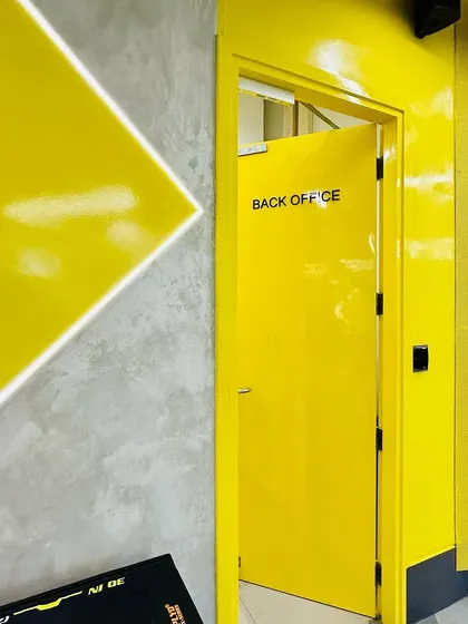 A detail shot showing the glossy yellow finish on the walls and doors, contrasted with the raw concrete texture. This interplay of materials adds visual interest and defines different functional areas like the back office.