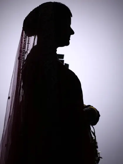A creative silhouette of a bride against a plain background, emphasizing her profile and traditional headwear.