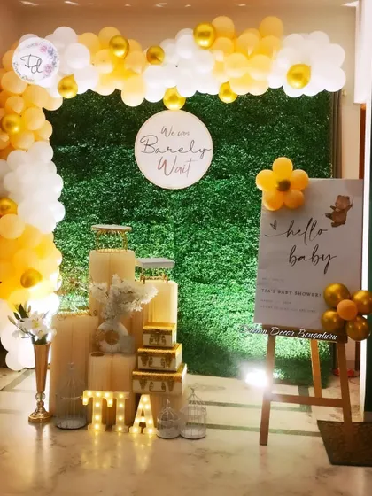A 'We can Bearly Wait' teddy bear-themed baby shower. The yellow and white balloon arch against a grass wall creates a bright and cheerful look.