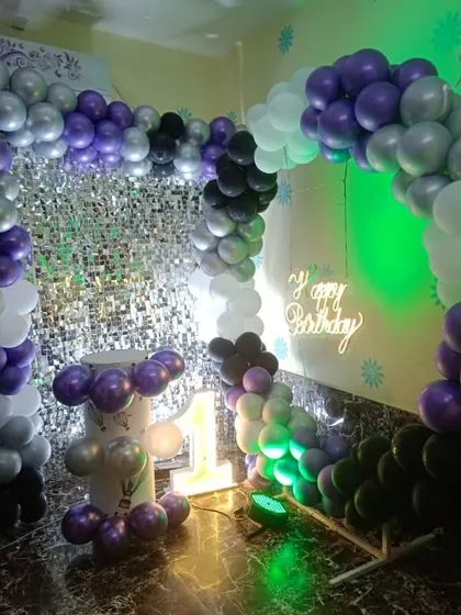 A full party setup with a silver shimmer wall and a balloon arch in purple, silver, and black, suitable for any age.