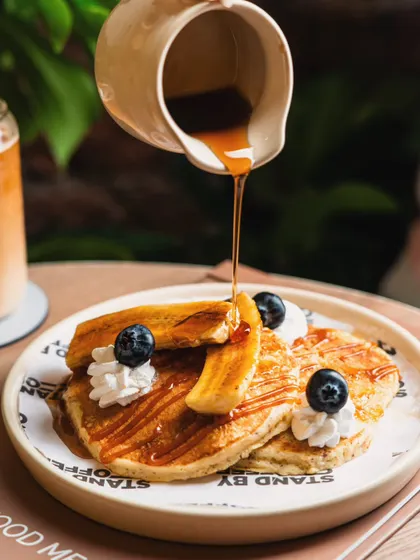 A thick stream of maple syrup being poured over a stack of pancakes. This classic action shot evokes a sense of indulgence and deliciousness.
