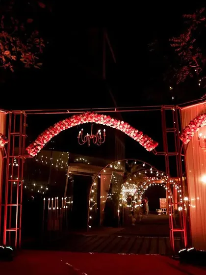 A grand entrance designed for a Sangeet night in Lonavala. The structure features red floral arches, classic chandeliers, and warm string lights, setting a dramatic and celebratory tone for an evening of 'Nacho Tappo'.