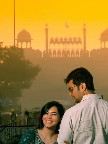 A beautifully composed pre-wedding shot with the Red Fort in the background, bathed in the warm light of a hazy sunset.