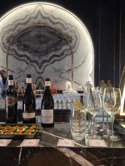 An elegant and modern bar setup featuring a striking marble backdrop. The display includes premium wines, spirits, and gourmet appetizers, creating a sophisticated station for guests to enjoy.