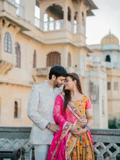 An intimate embrace between the couple, with their colorful traditional outfits popping against the neutral tones of the palace facade.