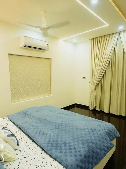 This bedroom features a clean and bright aesthetic, with light-colored curtains and recessed ceiling lights. The patterned wallpaper behind the bed adds a subtle touch of texture and interest.