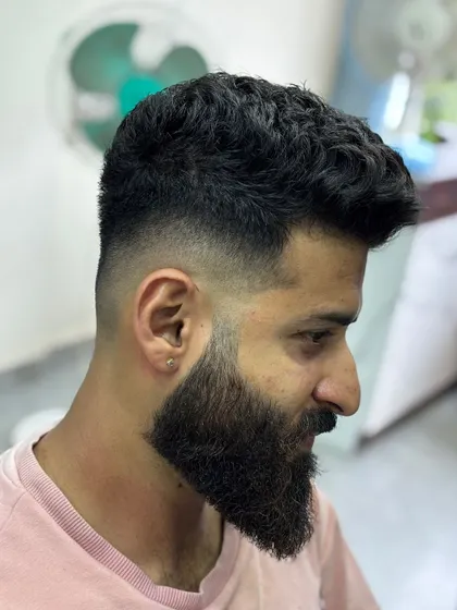 A high skin fade paired with a full, well-groomed beard. The contrast between the sharp fade and the textured beard creates a strong, masculine look.