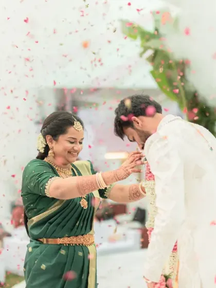 The mother of the groom adjusts his garland amidst a shower of petals. This is a beautiful, candid moment capturing a mother's love and blessings.