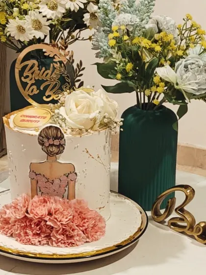 A chic and modern cake for a bride-to-be. This design features a custom illustration, fresh flowers, and a gold acrylic topper, making it a stylish centerpiece for a bridal shower.