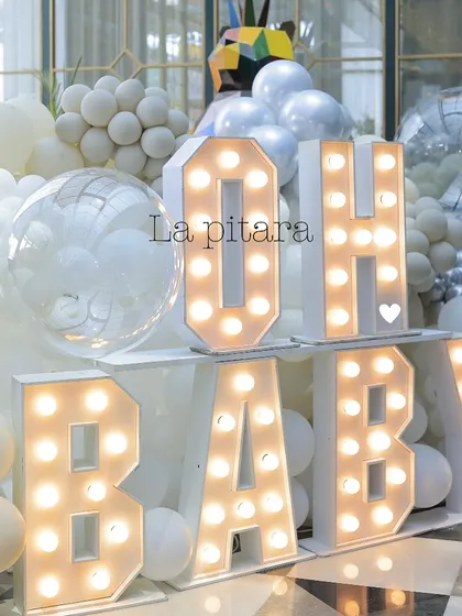 Large marquee letters spelling 'OH BABY' at an all-white baby shower, surrounded by a cloud of white and silver balloons.