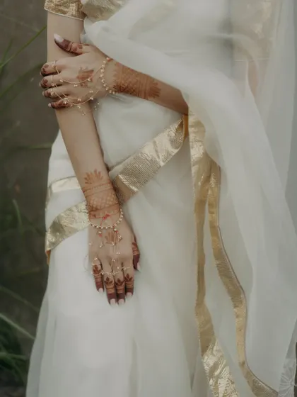 A detail shot of the bride's arms, adorned with delicate hathphool and mehendi, against her white and gold saree.