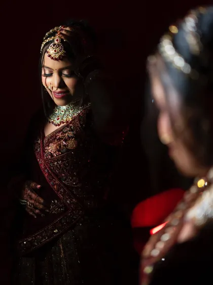 An over-the-shoulder shot of the bride looking into a mirror. This perspective creates a sense of intimacy, as if we are sharing a private moment with her.