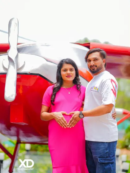 A happy couple's portrait in front of a vintage airplane, with their hands forming a heart on the baby bump.