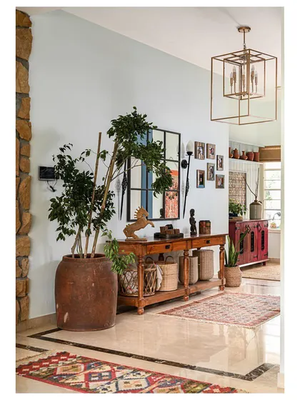 The foyer of the "Far From The Stone Street" home, featuring a long console table, a large terracotta pot, and a collection of rugs that set a warm, vintage tone.