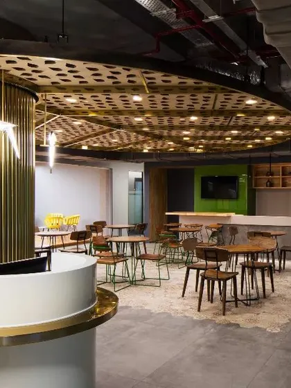 The cafeteria at the Okhla office, designed as a social hub with a distinctive circular theme. The brass-finished central column and varied seating arrangements create a dynamic and inviting space for breaks and informal meetings.