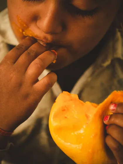 An extreme close-up of a child enjoying a mango, with juice smeared on their face. This shot is all about the messy, uninhibited joy of summer.
