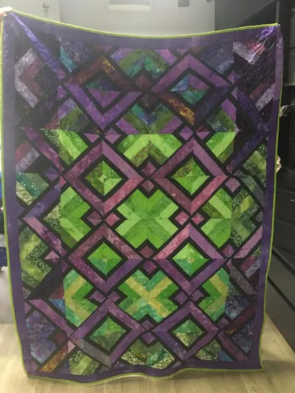 A complex geometric quilt in shades of purple and green, creating a stunning, almost kaleidoscopic effect.