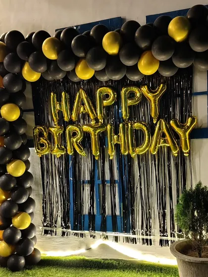 A simple yet bold birthday photo corner with a black and gold balloon frame against a black fringe curtain.