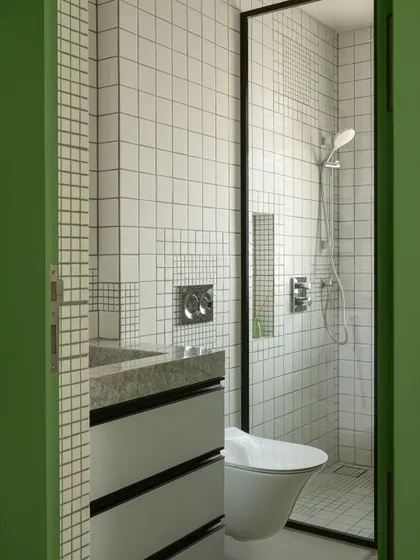 A view into the son's bathroom, where a grid of white tiles is playfully interrupted by smaller, pixel-like green tiles, creating a subtle graphic effect.