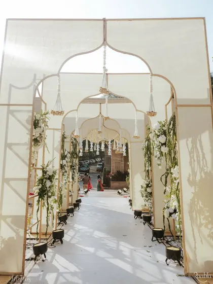 A grand arched entranceway for Aashvi and Akash's wedding, decorated with delicate white floral arrangements and hanging tassels. This created a soft and timeless passage into the main ceremony area.
