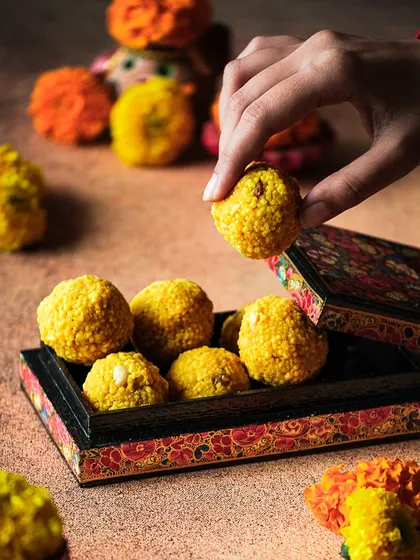 A close-up shot of a hand picking a ladoo from a beautifully painted box, capturing the essence of sharing sweets during Diwali.