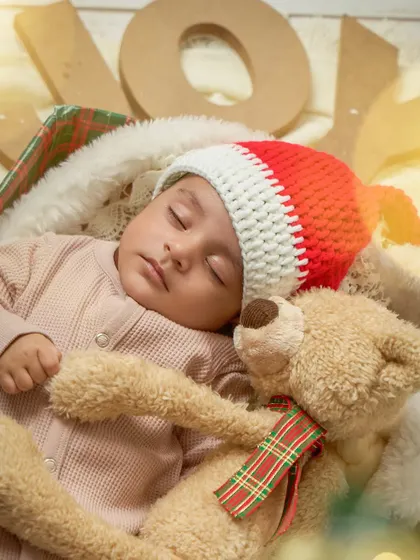 A newborn sleeps peacefully with a teddy bear during a Christmas mini session. The Santa hat and festive details make this an incredibly sweet 'baby's first Christmas' portrait.