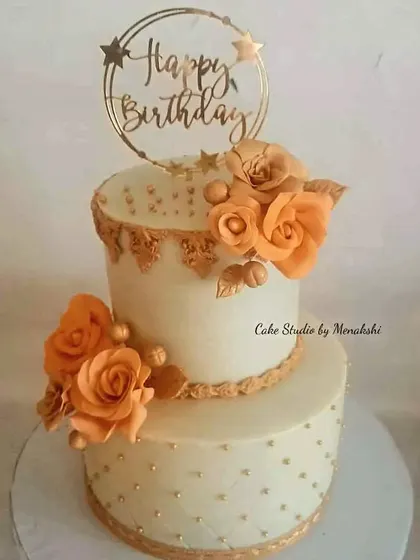 A grand two-tier birthday cake decorated with handmade orange sugar roses and delicate gold piping. This design shows how we can create a luxurious look with minimal fondant.