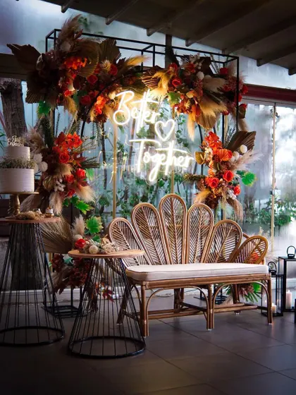 This "Better Together" setup combines industrial and boho elements. A black metal frame is softened with a rattan bench and lush, autumn-toned floral arrangements, creating a modern yet romantic photo spot.