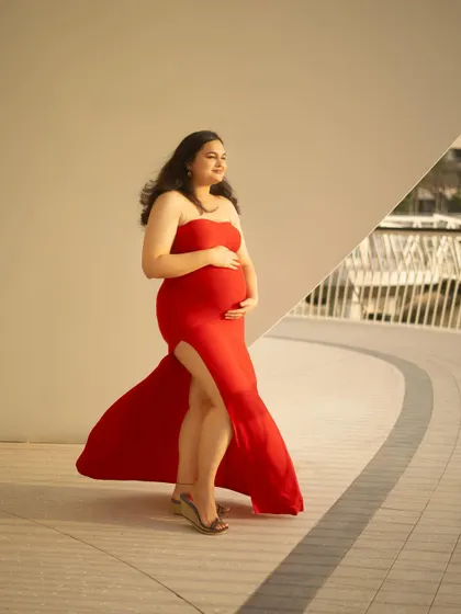 A beautiful profile shot that highlights the baby bump against a clean, architectural background. The slit in the red dress adds a touch of modern style to this outdoor portrait.