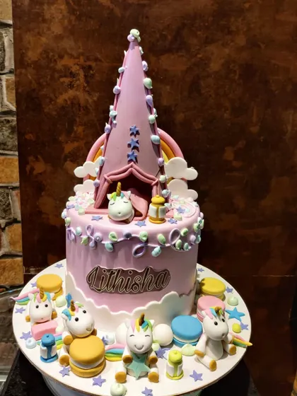 A closer look at my unicorn campsite cake. The design features a tall, pointed tent topper and several small, detailed unicorn figures enjoying a party at the base of the cake.