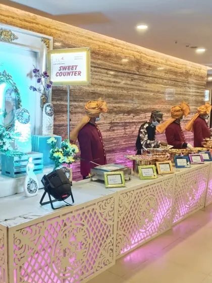 A vibrant sweet counter from a Sangeet ceremony. Our staff, dressed in traditional Rajasthani attire, are ready to serve a variety of delicious Indian desserts.