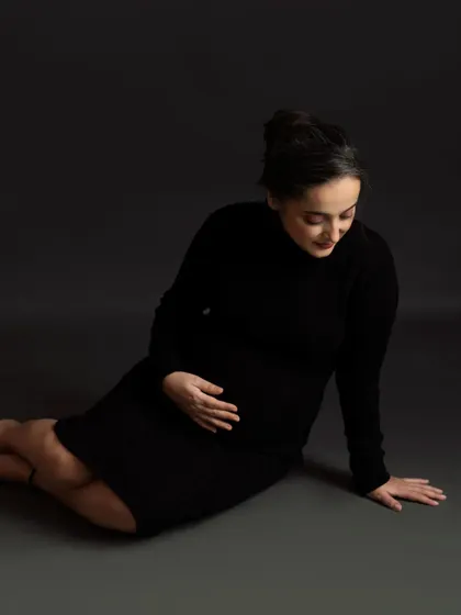 A quiet and beautiful solo portrait. The mom-to-be is seated, cradling her bump in a moment of peaceful reflection.