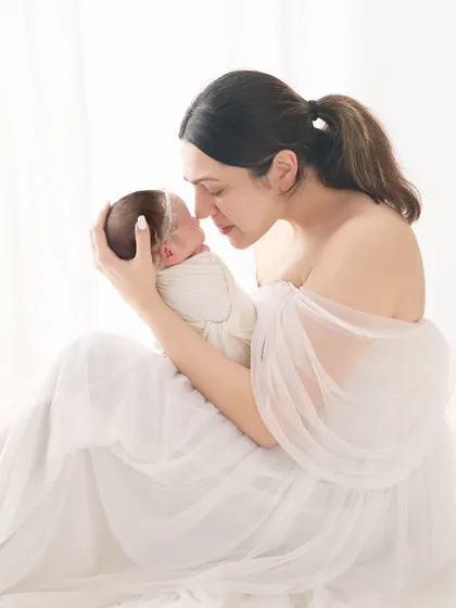 An intimate mother and child portrait, focusing on the gentle connection as she touches her nose to her baby's. The all-white styling creates a soft, ethereal feel, perfect for newborn photography.