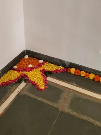 A floral rangoli design created with marigold petals in the corner of a room, adding a touch of traditional beauty to the indoor space.