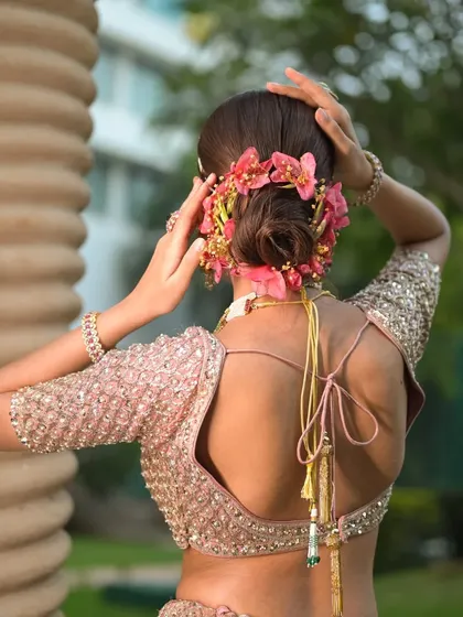 A back view of a romantic low bun adorned with a garland of vibrant pink orchids. This style is perfect for a destination wedding shoot or a spring fashion story.
