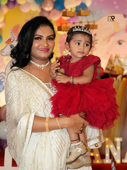A mother holds her daughter, both dressed beautifully for a special event. This photo captures a sweet moment between mother and child, showcasing their bond.