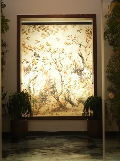 A wider shot of the illuminated peacock mural, showing how it acts as a stunning centerpiece in a hallway, enhanced by our plant styling.