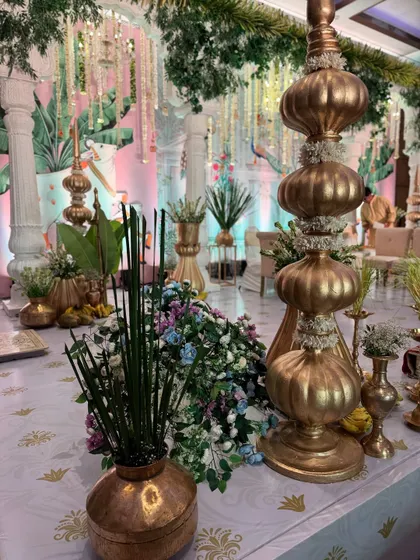 A detailed shot of a table setting at a Pichwai-themed wedding, featuring golden decor pieces, traditional banana offerings, and a backdrop of artistic paintings.