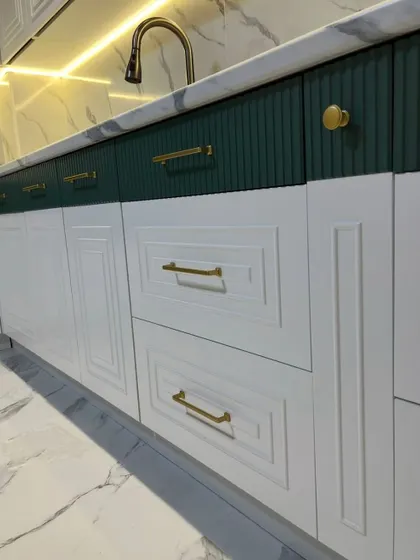 A close-up on the craftsmanship of our classic cabinets, showing the detailed moulding on the white doors and the vertical grooves on the green drawers, paired with elegant gold hardware.