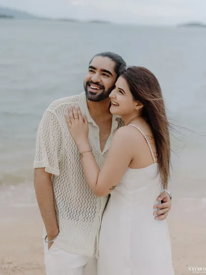 A windswept, happy portrait of a couple on the beach in Thailand, full of life and natural smiles.