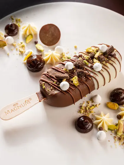 An exquisitely styled Magnum ice cream bar. The careful placement of chocolate curls, nuts, and meringues elevates the product into a gourmet dessert experience.