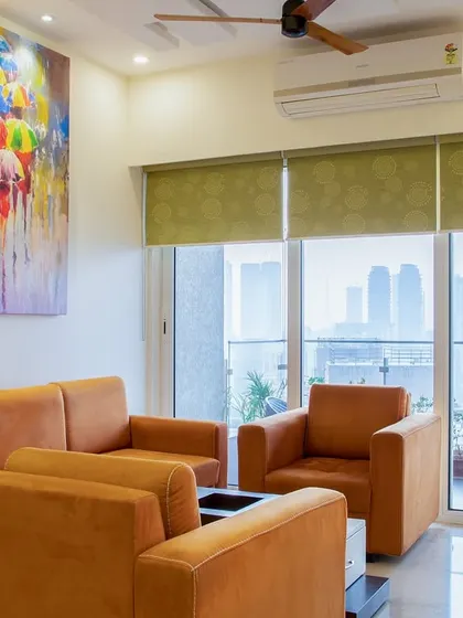 The living room offers a stunning city view, with the orange sofa providing a cheerful contrast to the neutral walls and green blinds.