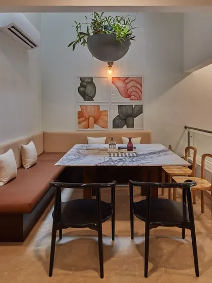 This cozy dining nook utilizes built-in L-shaped seating to maximize space. The combination of a marble-topped table, mixed-style chairs, and contemporary art creates a casual yet stylish corner for meals.