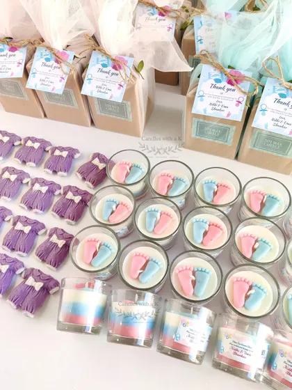 A closer look at the components for a baby shower order. You can see the detailed baby feet candles and the adorable purple baby onesie sachets before they are packed, highlighting the handmade quality of each item.