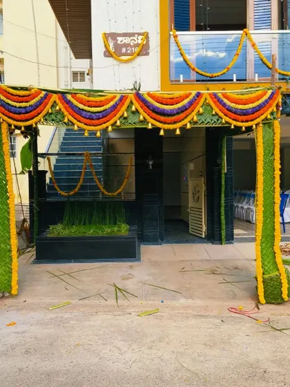 A daytime view of the housewarming chapra. The colorful flower garlands stand out beautifully against the green palm leaves.